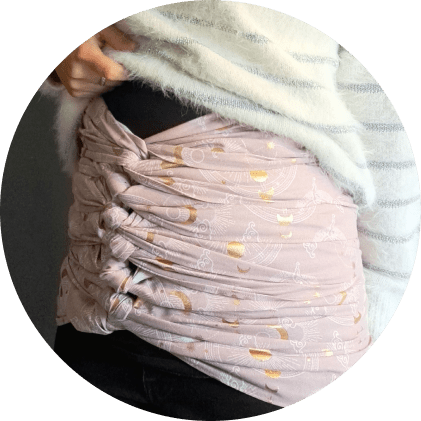 Femme habillée avec un tissu rose pâle élégamment noué autour des hanches, illustrant un bandage du ventre pour le post-partum.