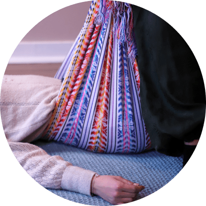 Femme allongée au sol avec le bassin enveloppé dans un tissu Rebozo, l’animatrice debout au-dessus d’elle effectuant le bercement du tissu.